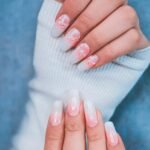 Close-up of hands showcasing elegant gradient nail art with floral designs.