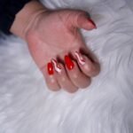 Elegant red and white nail design on hand resting on fluffy surface. Ideal for fashion and beauty concepts.