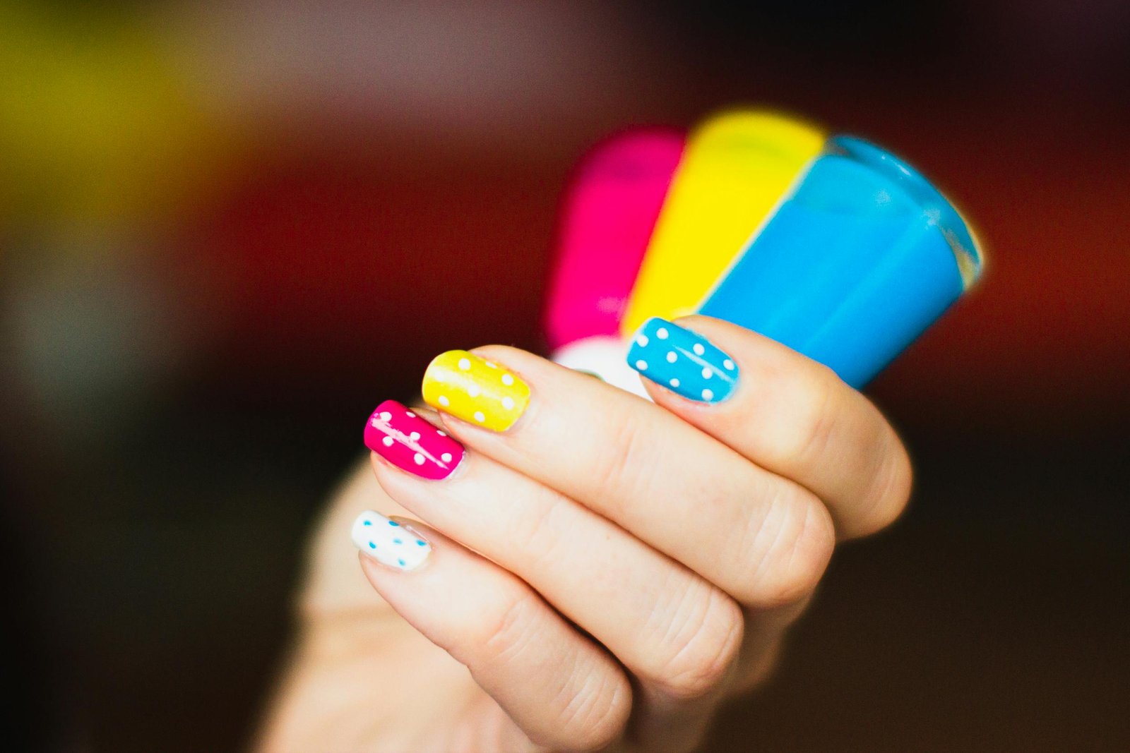 Close-up of a hand with colorful polka dot nail art holding vibrant nail polish bottles.